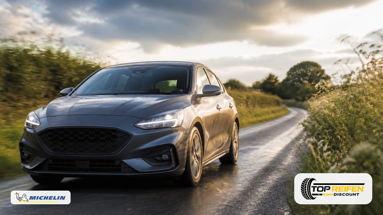 Car on a country lane after a brief summer shower, low road-level camera angle focusing on the front tyre; warm evening light on damp asphalt.