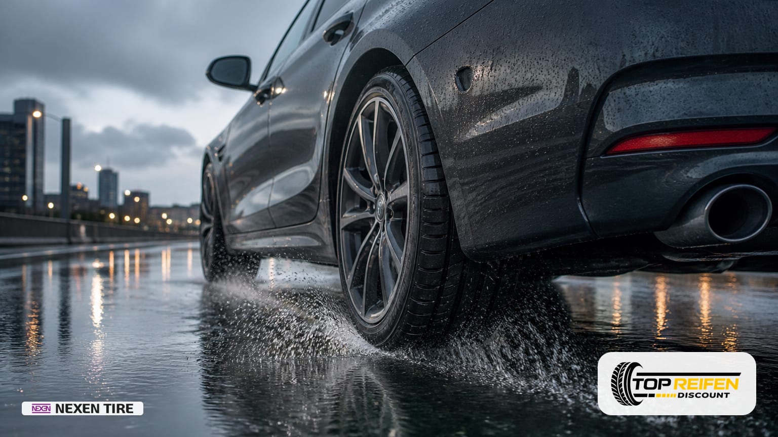 NEXEN NB-4S2 255/40 R19 bei Nässe: Rückansicht eines rollenden Reifens durch flaches Wasser, Sprühnebel und Spiegelungen auf nasser Fahrbahn unter grauem Himmel.