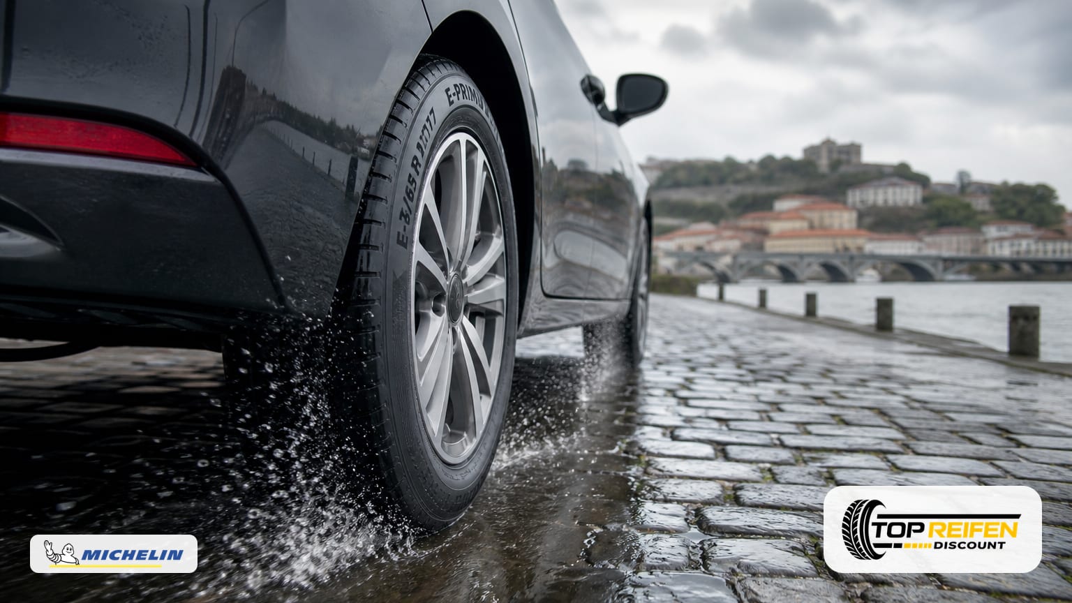 PKW mit MICHELIN E-PRIM 175/65 R17 rollt auf nasser Straße; Nahaufnahme des Hinterrads mit Wasserspritzern bei bedecktem Himmel.